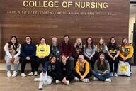 A group of students sit under a sign that says College of Nursing at the University of Wisconsin–Oshkosh